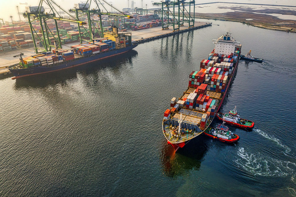 Container ship docked at a port with cranes and other ships in the background.