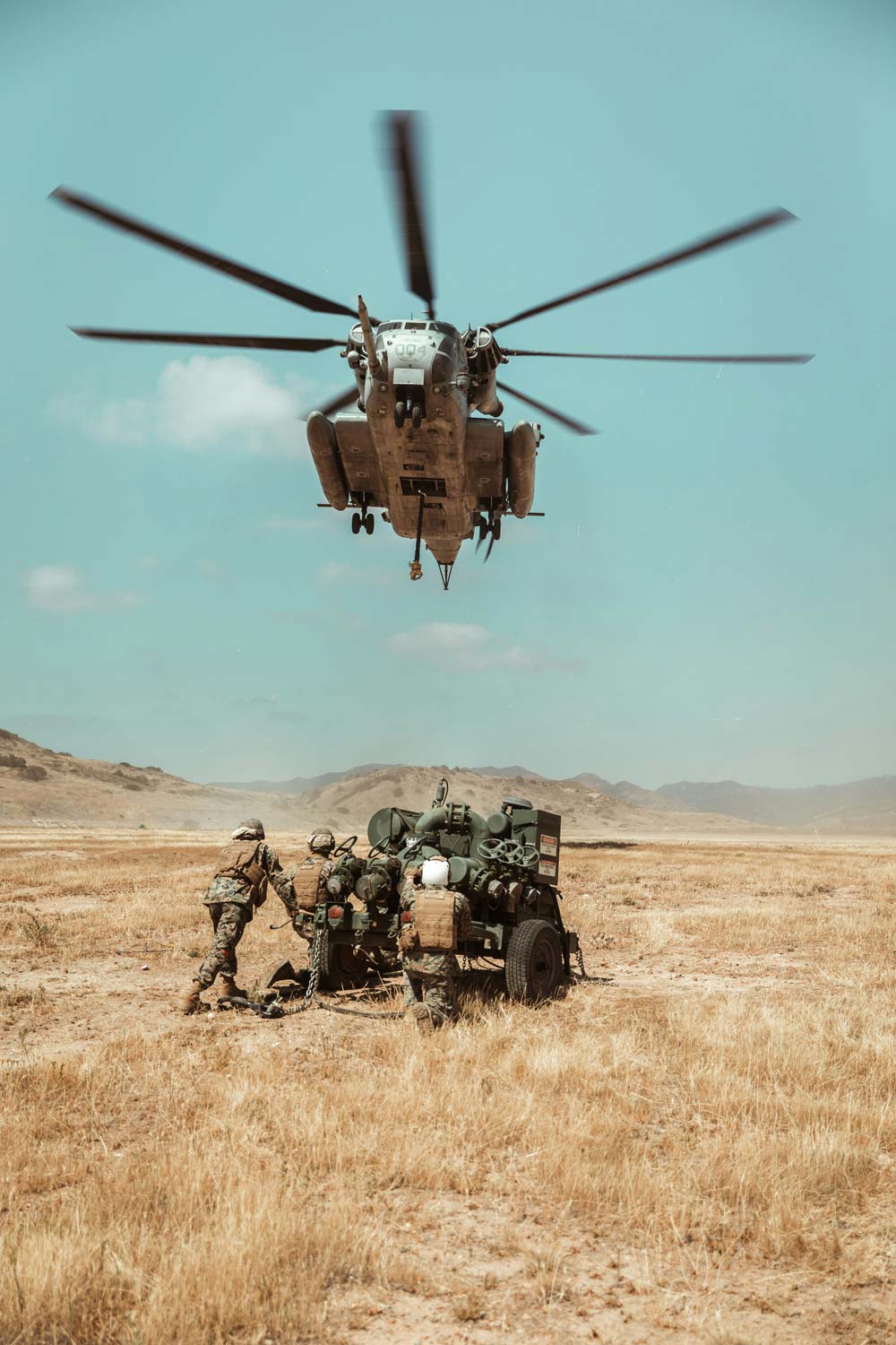 Helicopter flying over soldiers with equipment in a desert landscape
