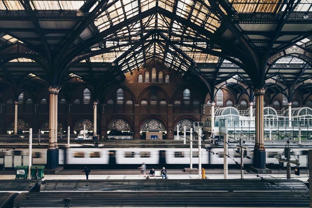 Large train station with high ceilings and a glass roof, featuring a train on the platform.